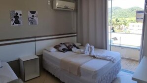 Habitación de hotel con cama, mesita de noche, escritorio pequeño y ventana con vistas a zonas verdes.