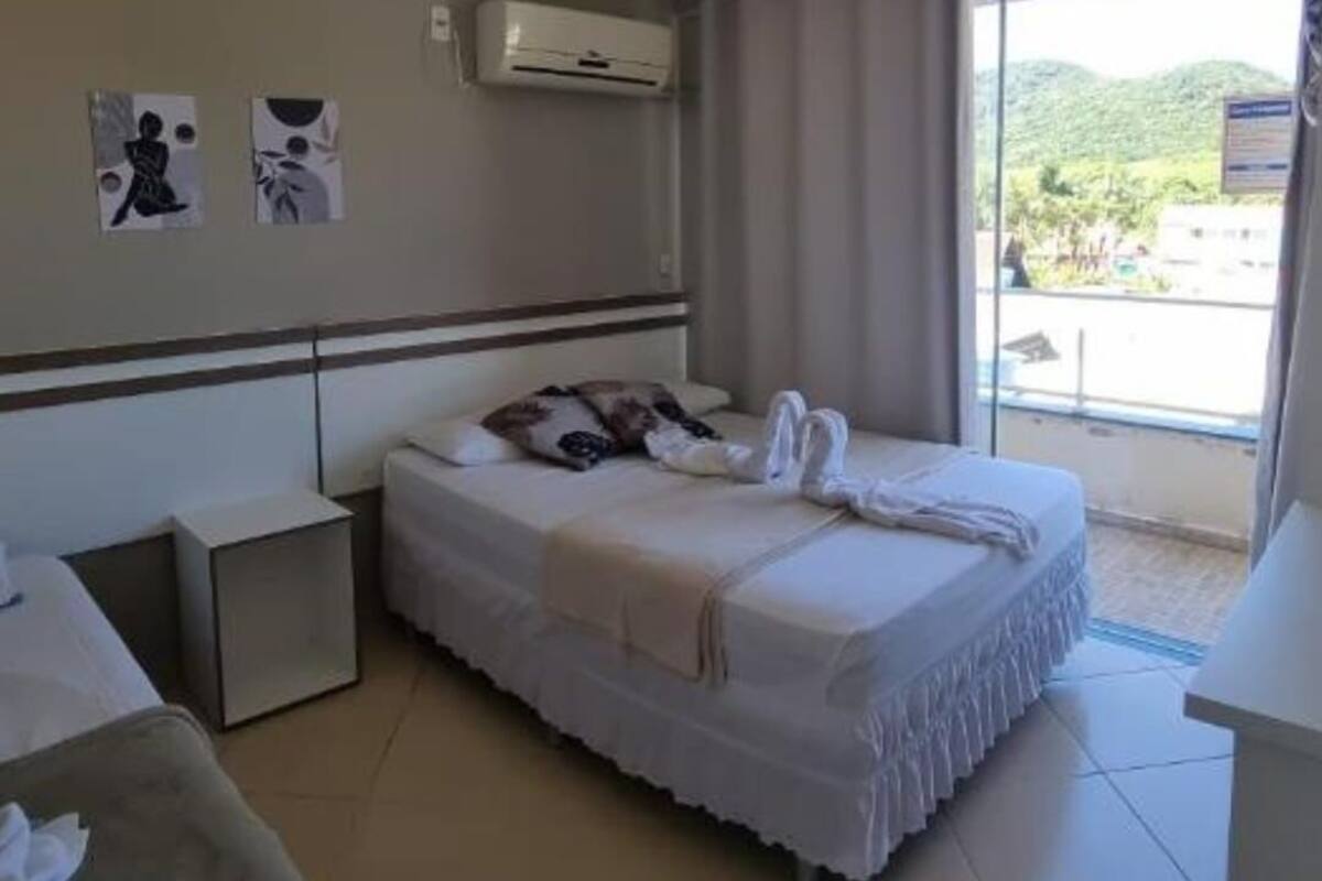 A hotel room with a bed, a bedside table, a small desk, and a window with a view of greenery.
