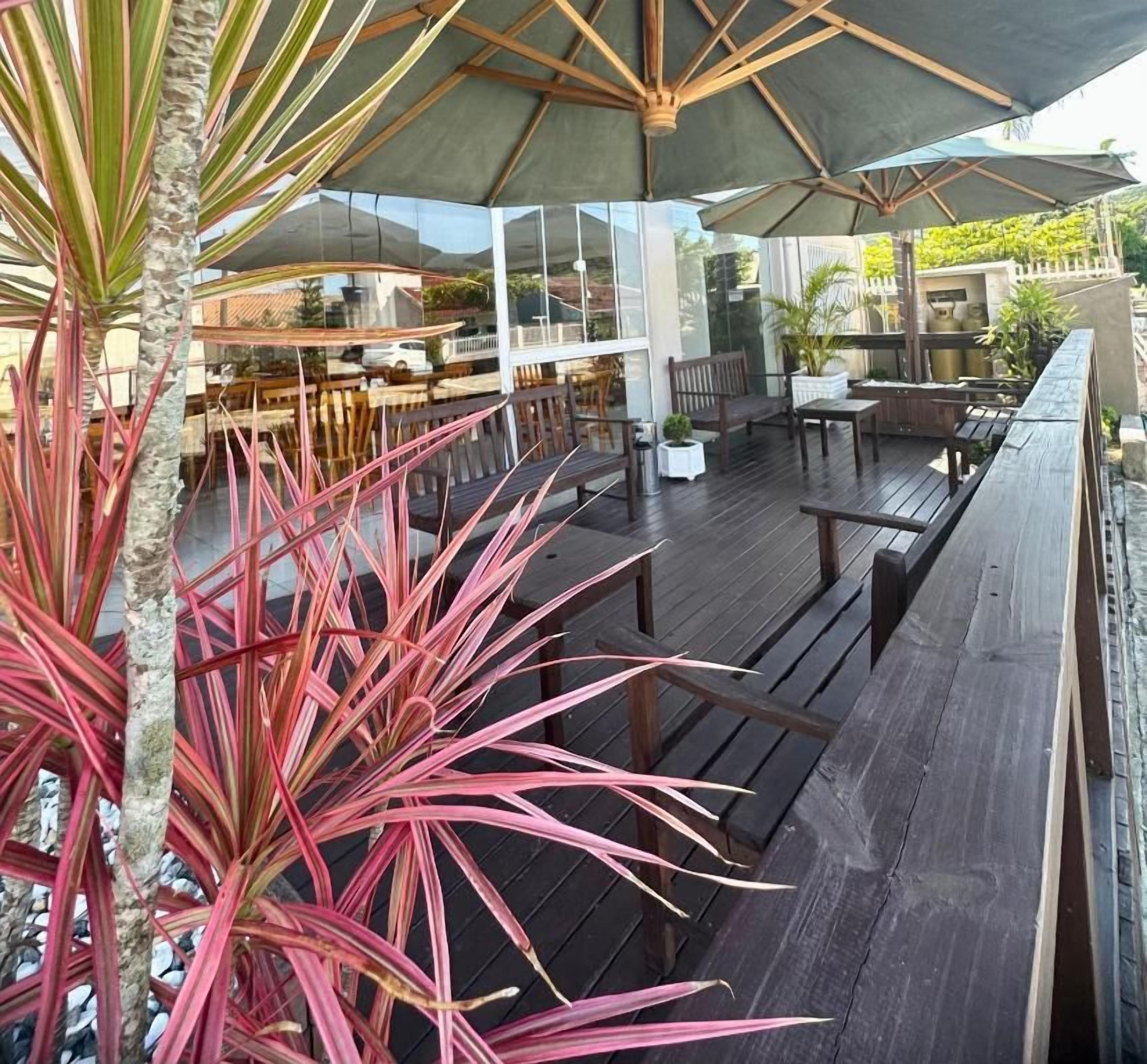 An outdoor seating area with wooden tables and chairs, a covered patio, and a view of the surrounding landscape.