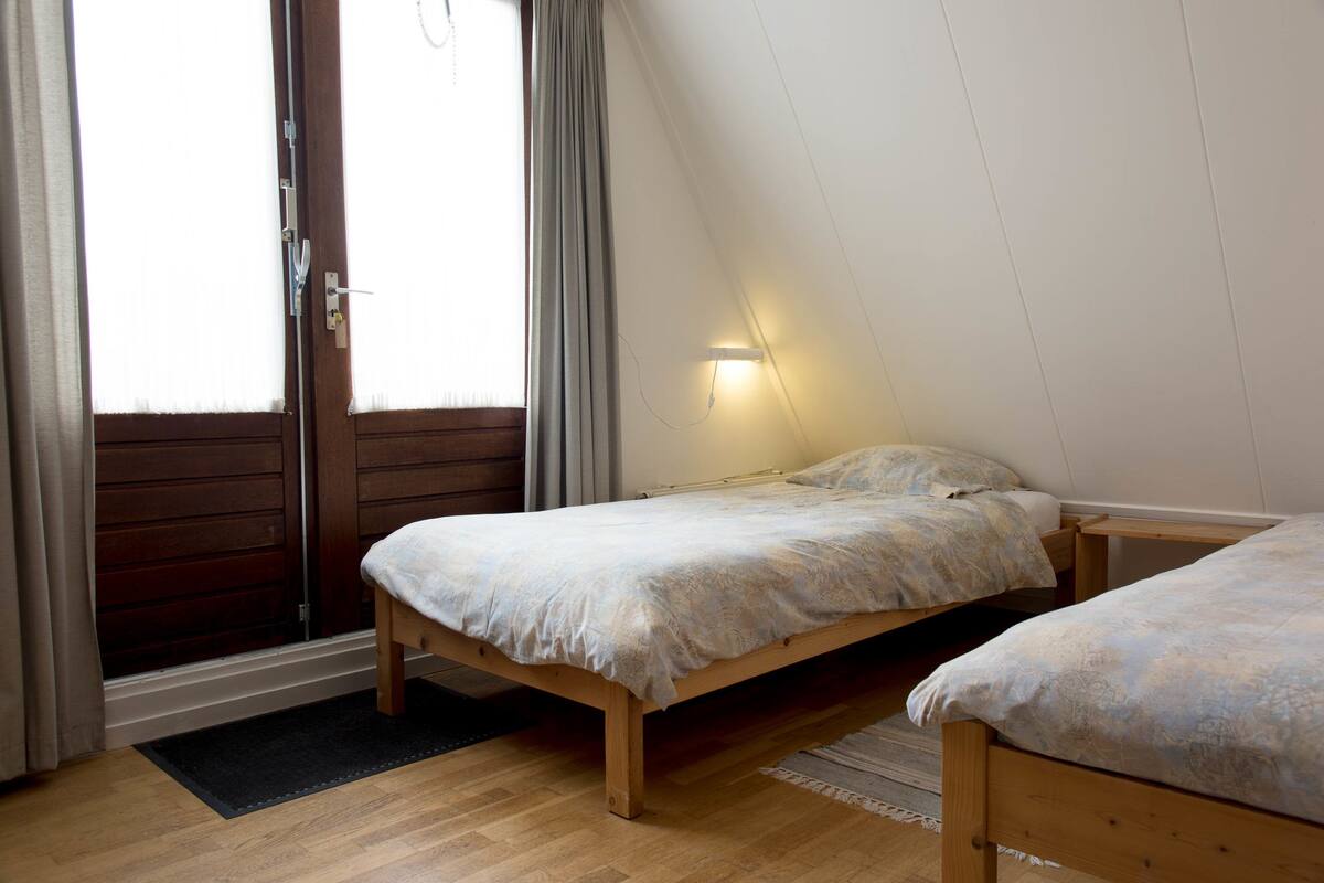 Ein Schlafzimmer mit einem hölzernen Bett, einem Fenster mit Vorhängen und einer Wandleuchte.