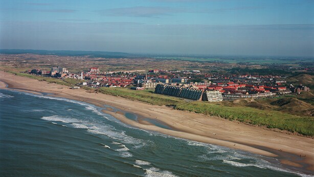 Un pueblo costero con una playa, edificios y un paisaje montañoso al fondo.
