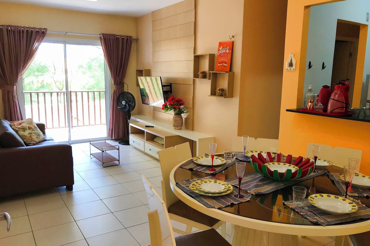 A dining area with a round table set for four, a sofa, a fan, and a TV on a stand.
