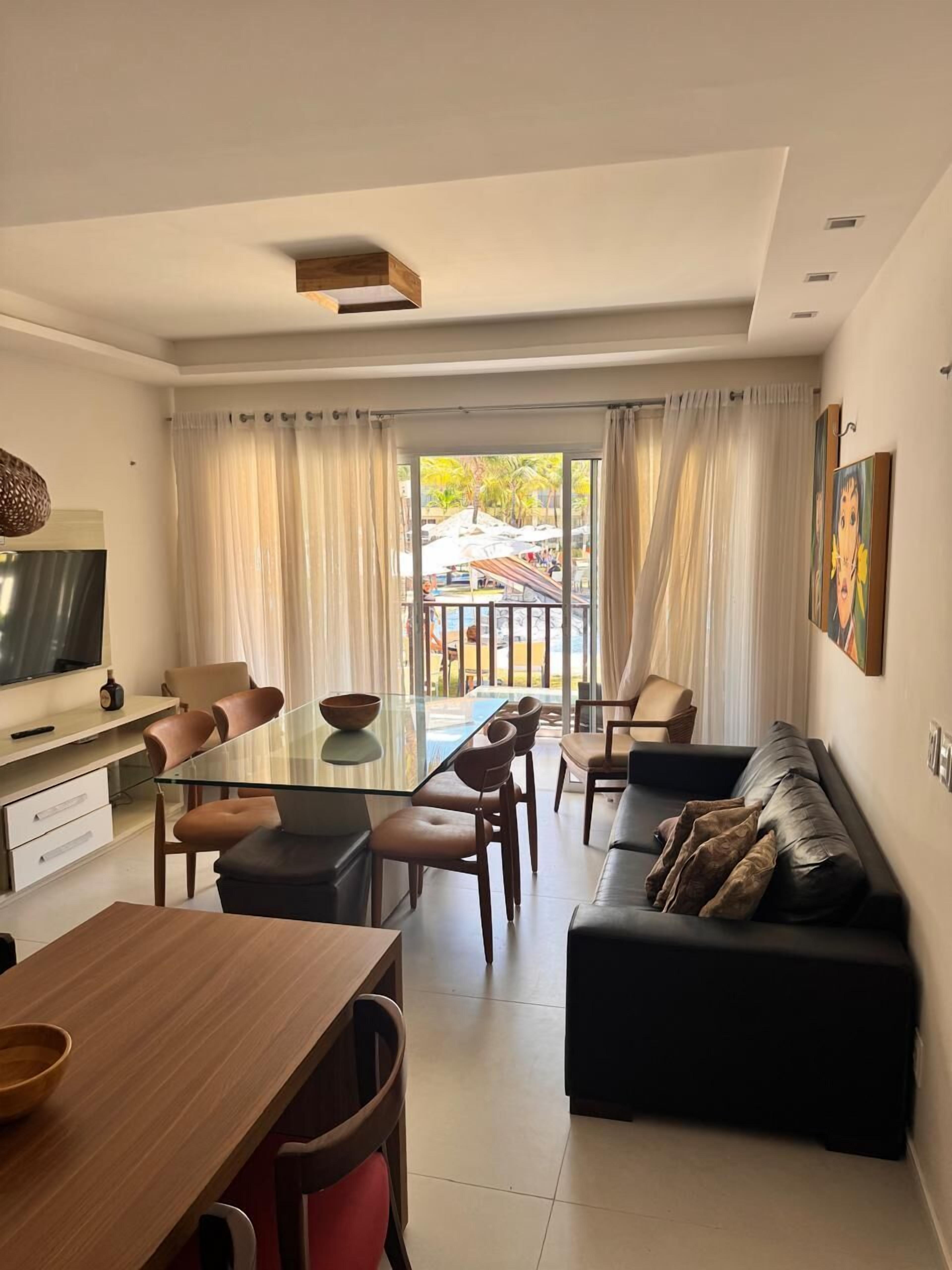 A modern living room with a glass dining table, leather sofa, and a TV on a stand.