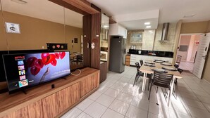 A modern kitchen with a built-in refrigerator, a dining area with a table and chairs, and a TV mounted on a wooden cabinet displaying a Netflix advertisement. - Beach Living, Frente mar, 400m do B Park (Aquiraz)