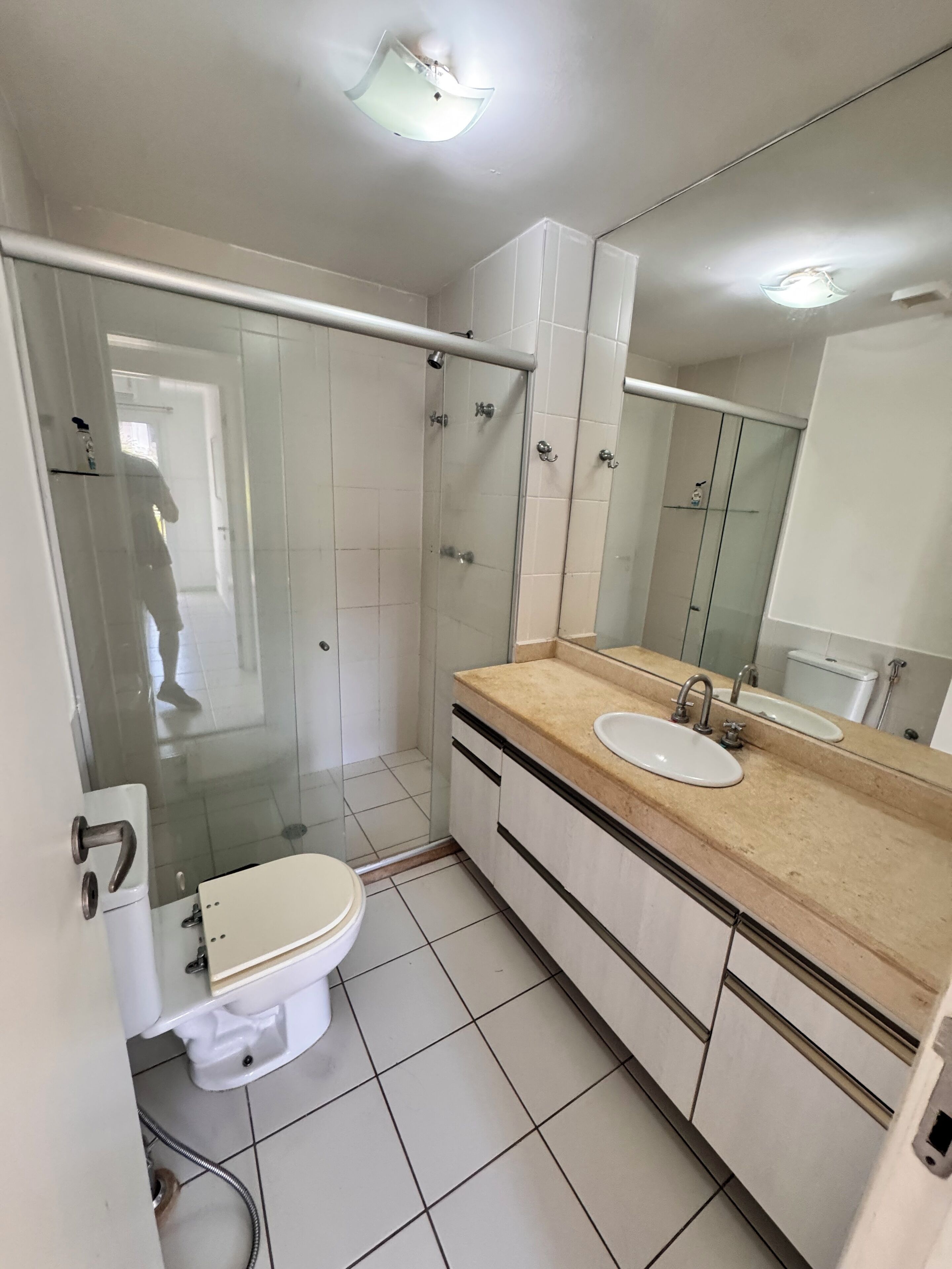A modern bathroom with a glass-enclosed shower, a white toilet, a sink with a beige countertop, and a large mirror.