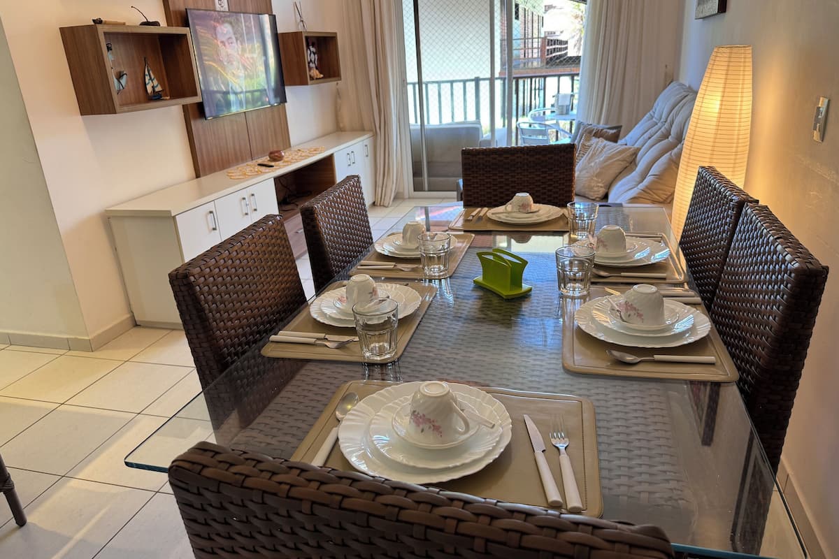 A dining area with a glass table, wicker chairs, and a buffet setup.