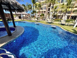 Una piscina con una estructura de techo de paja, rodeada de palmeras y sillas de descanso.
