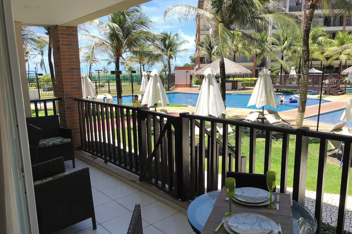 A balcony with a view of a swimming pool, lounge chairs, and umbrellas.
