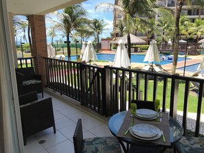 A balcony with a view of a swimming pool, lounge chairs, and umbrellas. - Beach living, Pé na areia, Vizinho ao B Park - Oficial (Aquiraz)