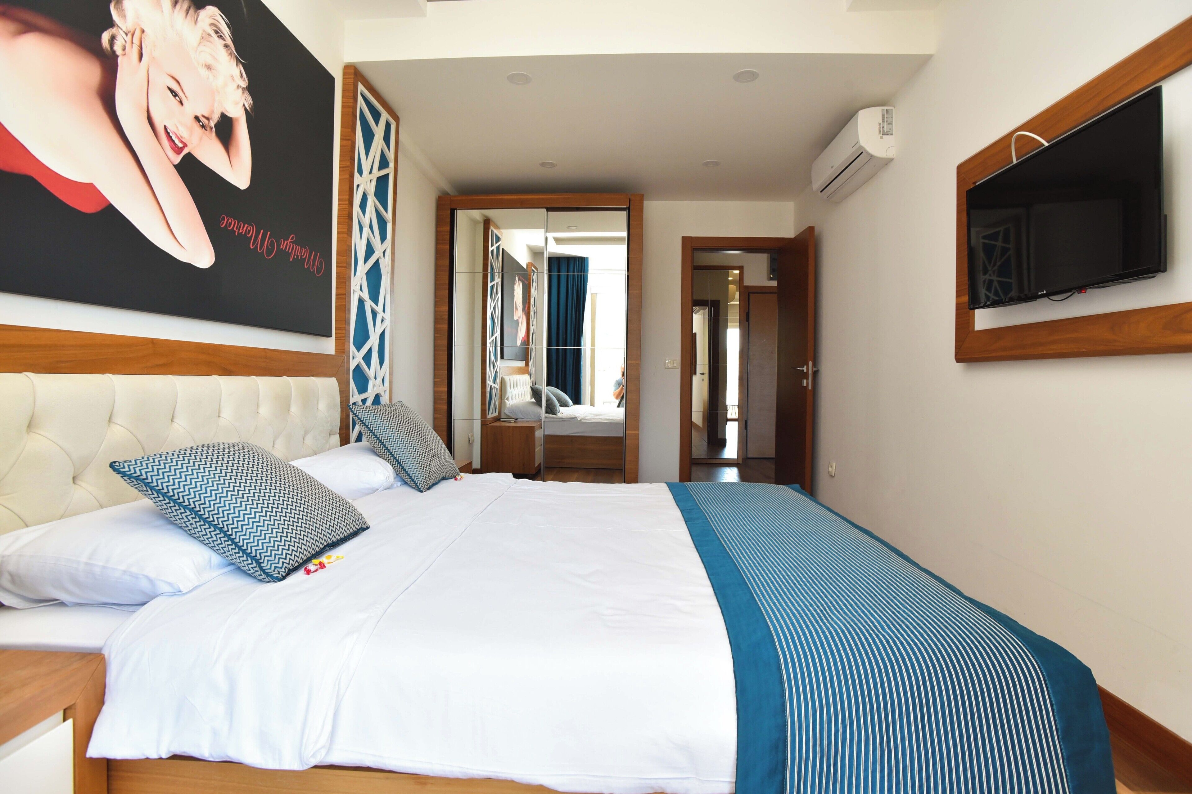 A bedroom with a large bed, a TV mounted on the wall, and a mirror above the bed.
