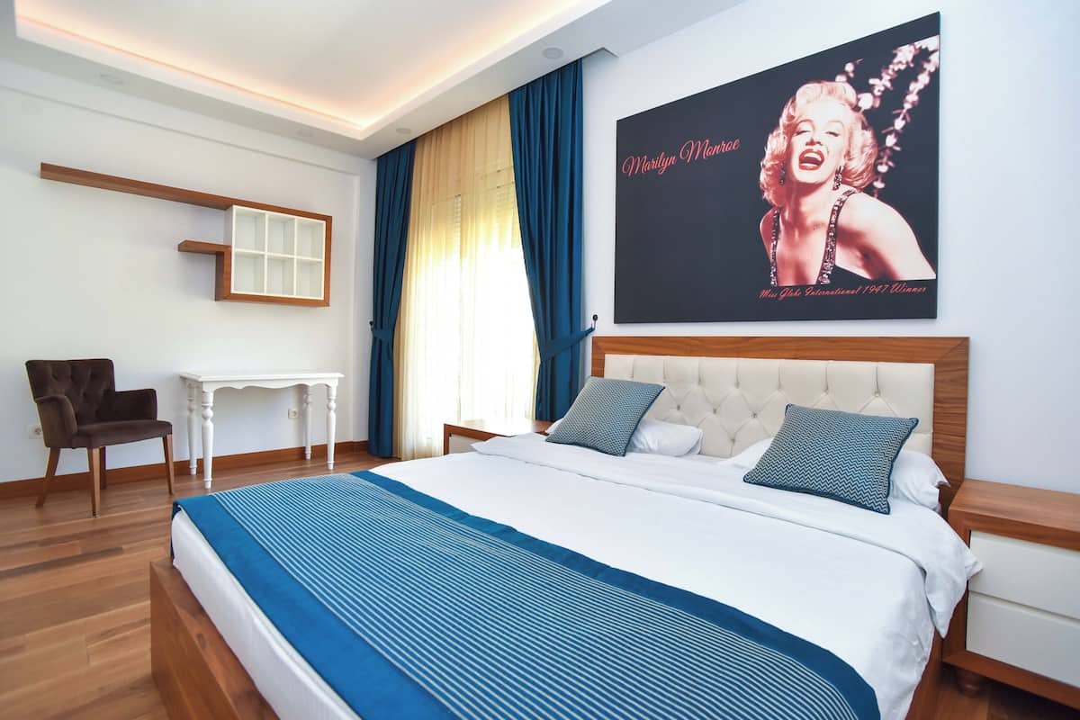 A hotel room with a large bed, a small table, a chair, and a poster on the wall.