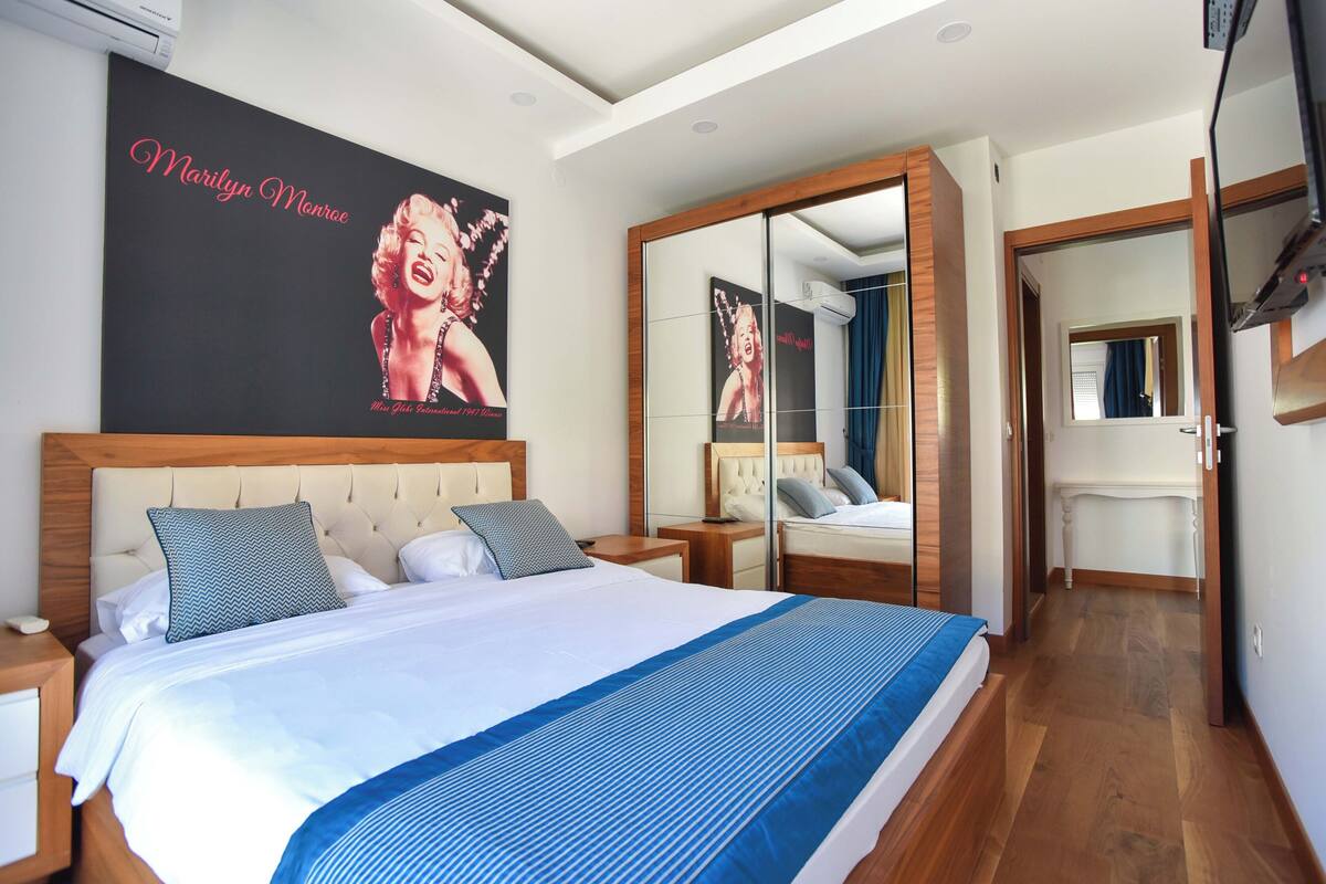 A hotel room with a large bed, a mirror, a poster of Marilyn Monroe, and a TV.