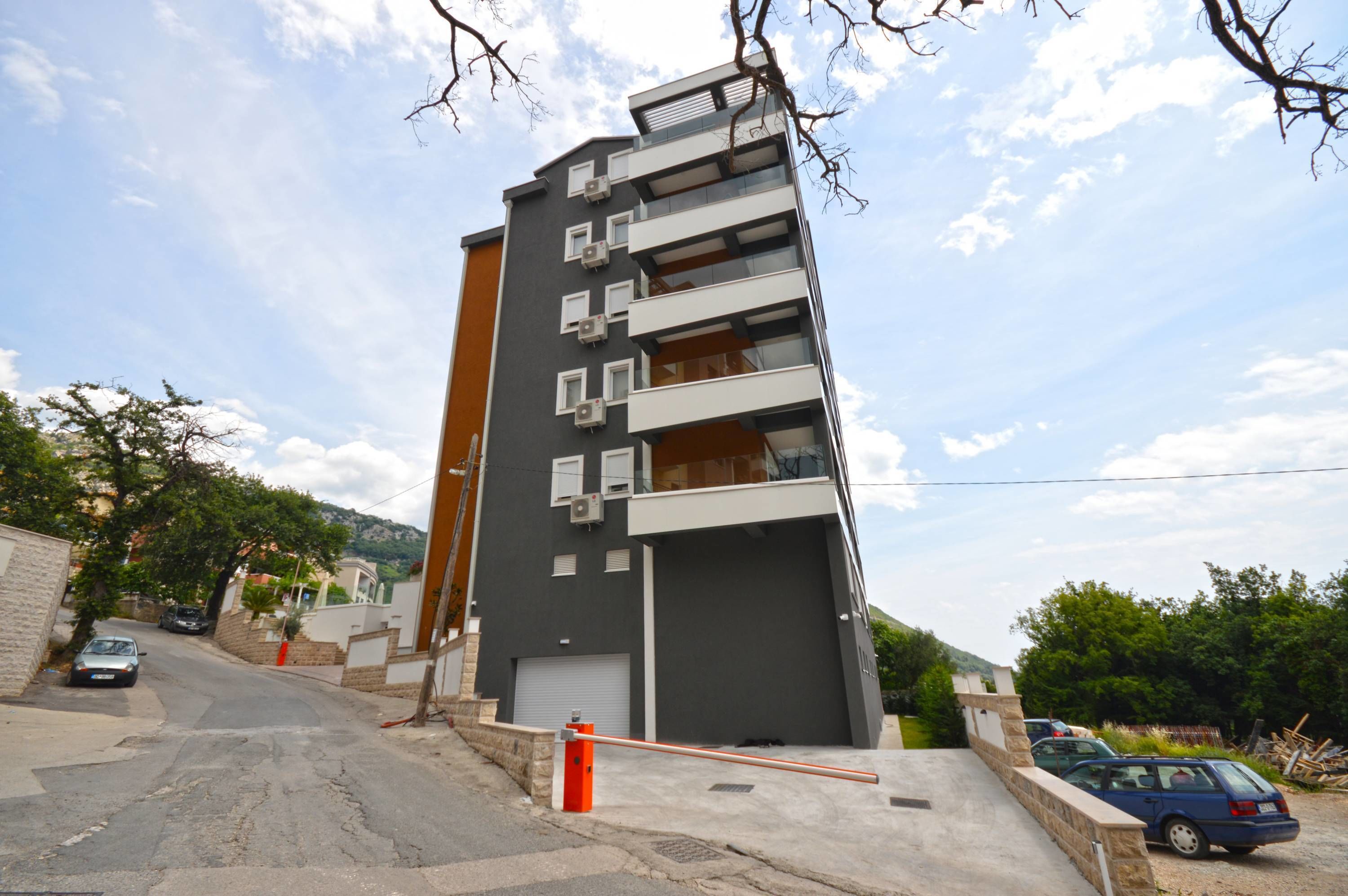 A modern multi-story building with balconies, a garage, and a parking area.
