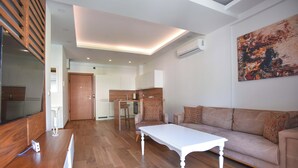 Un salón moderno con suelo de madera, una mesa de centro blanca, un sofá beige y un televisor a la izquierda.
