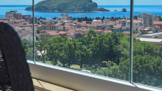 Un balcón con vista a un pueblo costero, una silla y una ventana.