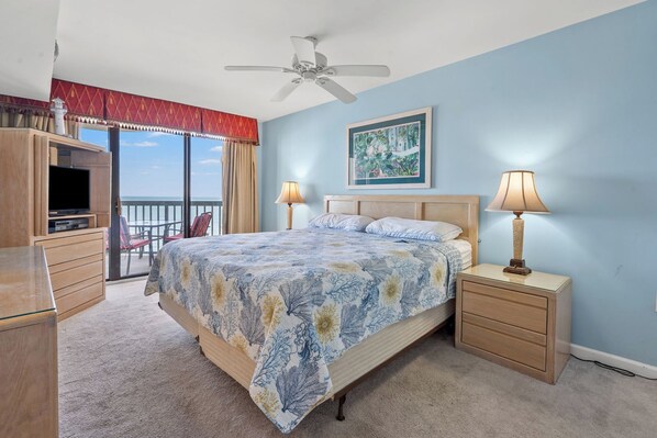 A bedroom with a bed, two bedside tables, a ceiling fan, a TV, and a balcony with a red curtain.