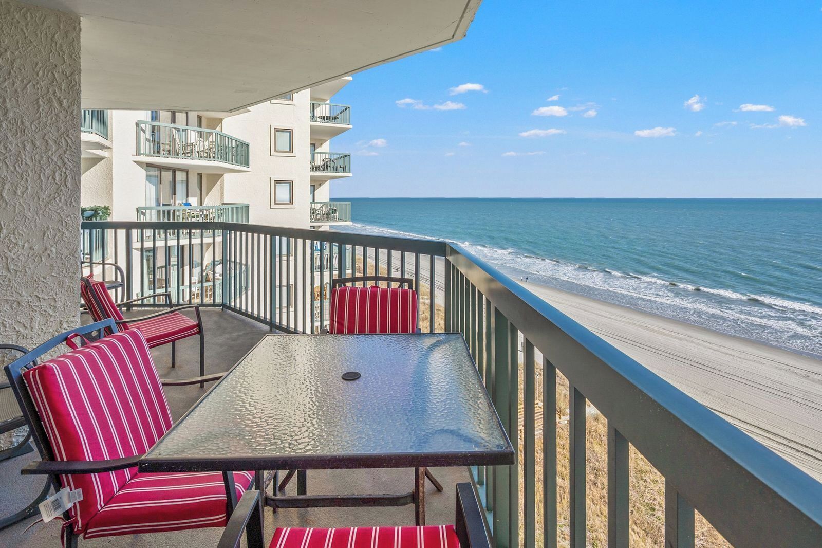 Un balcon avec une table et des chaises, donnant sur une plage où l’on peut voir les vagues.