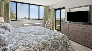 Une chambre avec un grand lit, une télévision, une commode et une vue sur l’océan.