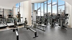 Une salle de sport moderne équipée de tapis de course, d’appareils de musculation et dotée d’une grande fenêtre offrant une vue sur la ville.