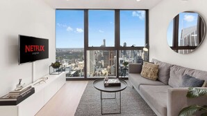 Un salon moderne doté d’une grande fenêtre, d’un téléviseur à écran plat, d’un canapé, d’une table basse et offrant une vue sur la ville.