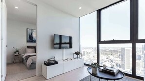 Un salon moderne doté d’une grande fenêtre, d’un téléviseur à écran plat, d’une console blanche et offrant une vue sur la ville.