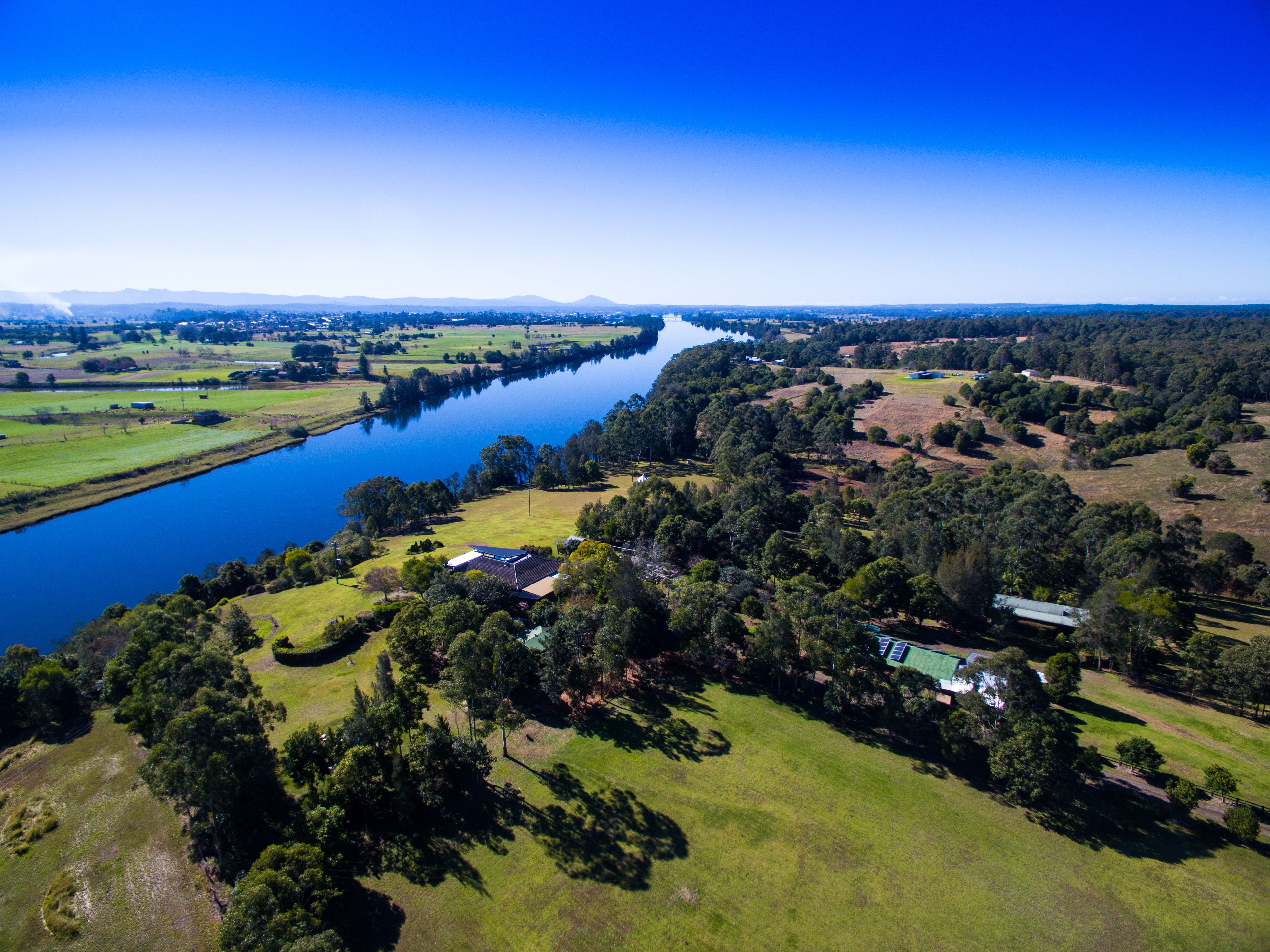 An aerial view of a rural area with a river, green fields, and scattered houses.