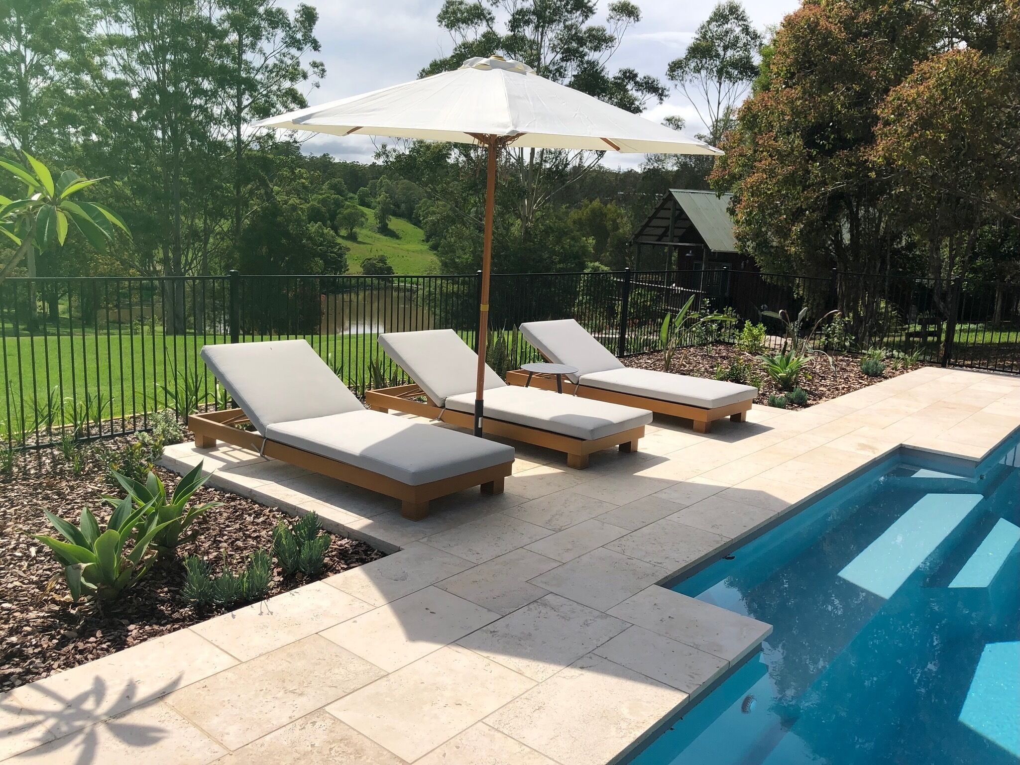 A poolside area with three lounge chairs and a large umbrella.