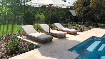 A poolside area with three lounge chairs and a large umbrella.