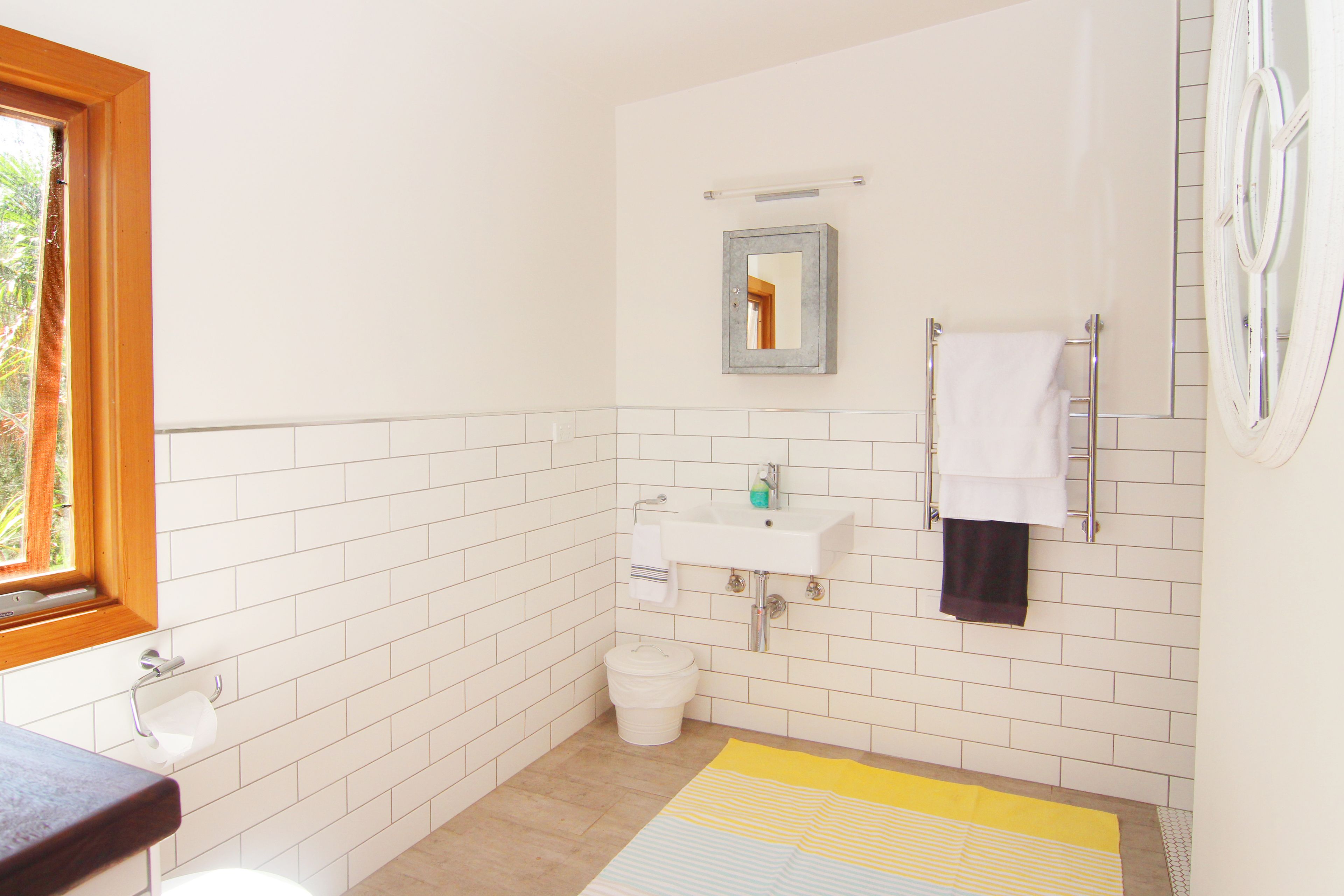 A bathroom with white tiled walls, a sink, a mirror, a toilet, and a window.