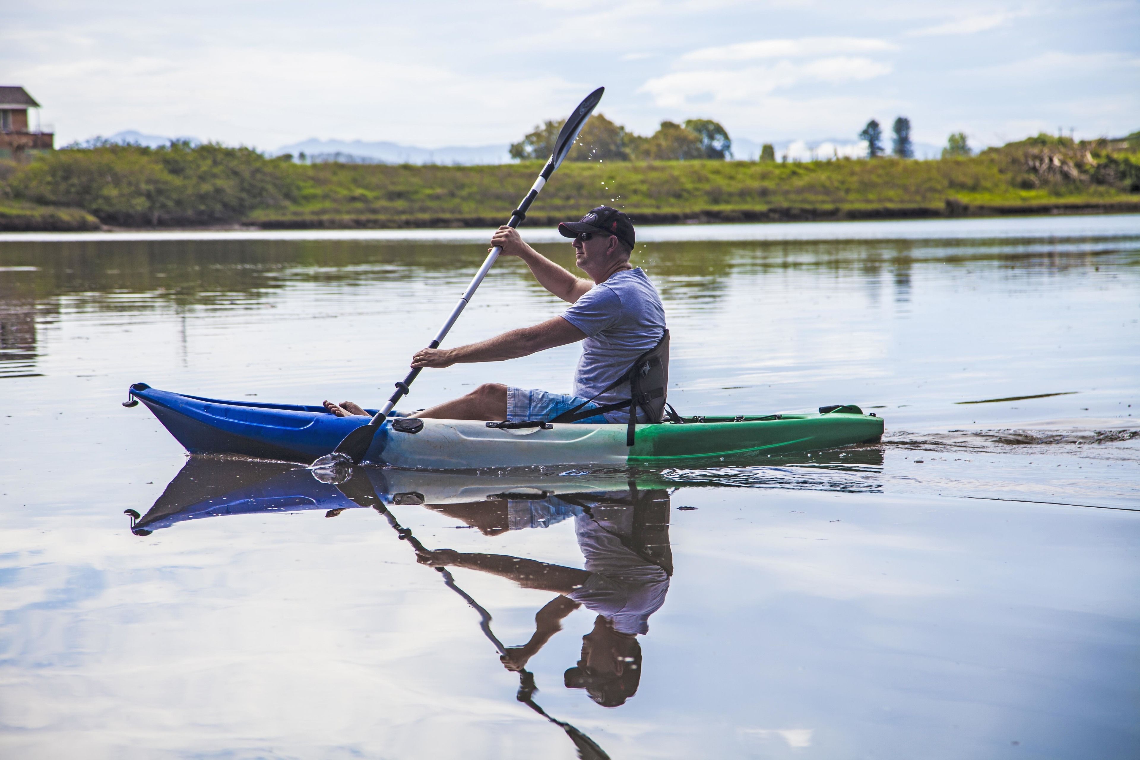 A person rowing a green and blue kayak on calm water.