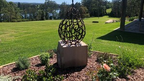 A metal sculpture in a garden with a clear view of a lake and trees in the background. - Mansfield on the Manning (Tinonee)