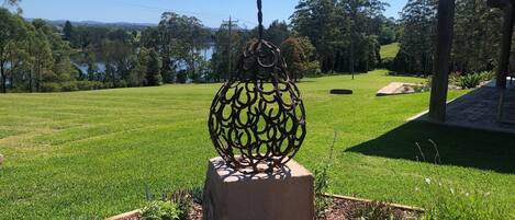 A metal sculpture in a garden with a clear view of a lake and trees in the background.