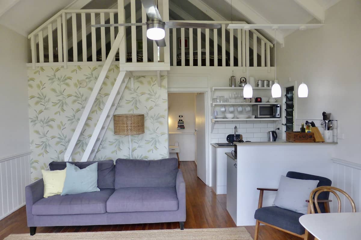 A cozy living room with a purple sofa, a wooden dining table, and a kitchen area with a microwave and shelves.