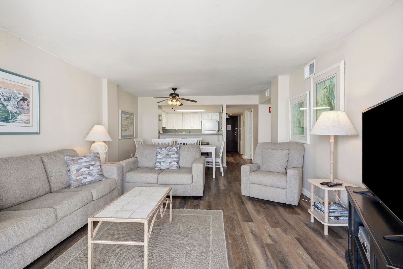A living room with a sofa, armchairs, a coffee table, a TV, and a ceiling fan.