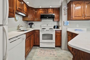 A compact kitchen with wooden cabinets, a white stove, and a stainless steel microwave.