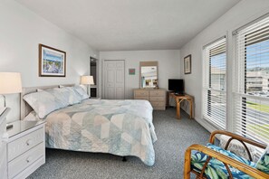 A bedroom with a bed, dresser, TV, and a chair.