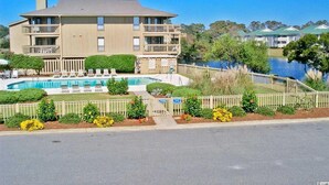 A two-story building with a swimming pool, surrounded by a fence and landscaped garden. - Tilghman Lakes By the Sea (North Myrtle Beach)