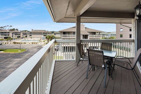 A balcony with a table and chairs, overlooking a parking lot and buildings.