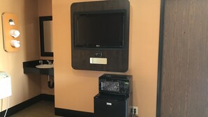 A hotel room with a black TV mounted on the wall, a small black refrigerator, a sink with a black countertop, and a wooden door. - El Rancho Motel (Los Angeles)