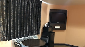 A room with a round table, two chairs, a black air conditioner, a black refrigerator, and a mounted television. - El Rancho Motel (Los Angeles)