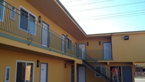 A yellow building with a covered outdoor area, a staircase, and multiple doors. - El Rancho Motel (Los Angeles)