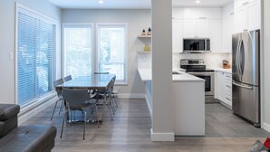 A modern kitchen with white cabinets, stainless steel appliances, and a dining area with a table and chairs. - Painted Cliff 18  Ski-in, Ski-out Luxury with serene mountain view, sleeps 7 (Whistler)