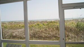 A view through a window with a wooden fence in the foreground and a beach in the background. - Sea Cloisters I Ocean Front Beach Retreat (North Myrtle Beach)