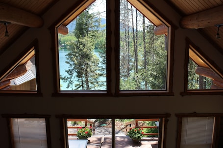 A room with large windows overlooking a forest and a lake.