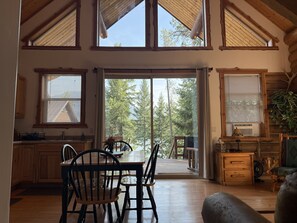 A spacious cabin interior with a dining area, kitchen, and large sliding glass doors leading to a deck.