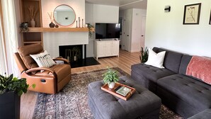 A modern living room with a fireplace, leather armchair, grey sofa, and a flat-screen TV. - Town & Country Cottage. Located in the heart of Intercourse, Pa. (Ronks)