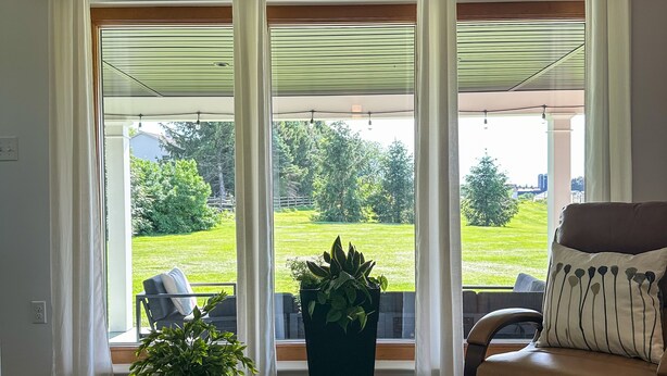 A living room with a grey sofa, a brown armchair, a large window with sheer curtains, a potted plant, and a tray with a book and remote control. - Town & Country Cottage. Located in the heart of Intercourse, Pa. (Ronks)