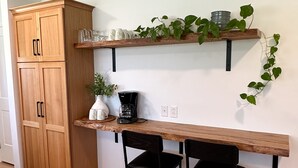 A kitchen with wooden cabinets, a coffee maker, two black chairs, and a plant on a shelf. - Town & Country Cottage. Located in the heart of Intercourse, Pa. (Ronks)
