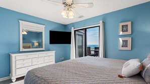 A bedroom with a large bed, a dresser, a ceiling fan, a TV, and a view of the ocean. - Sea Cloisters II Ocean Front Beach Retreat (North Myrtle Beach)