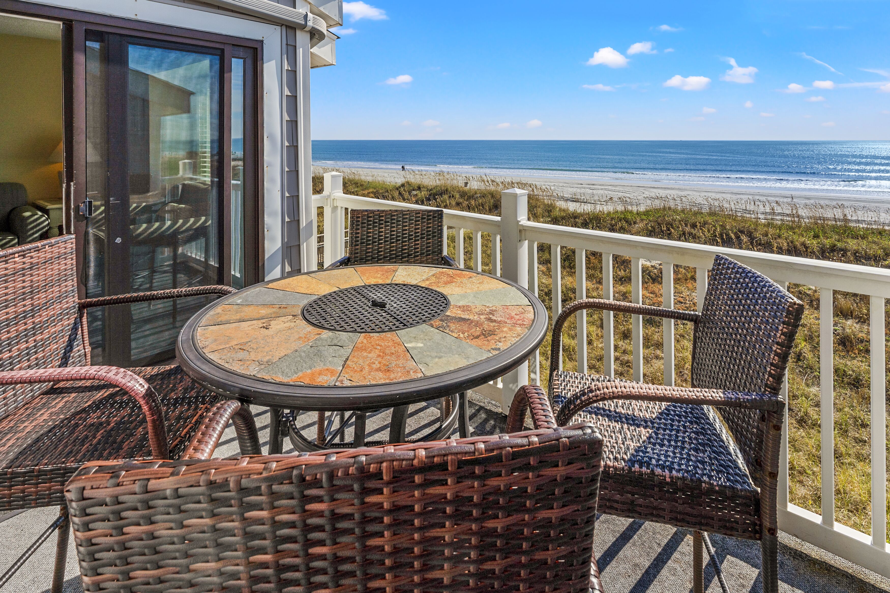 A balcony with wicker furniture and a glass door leading to a room.